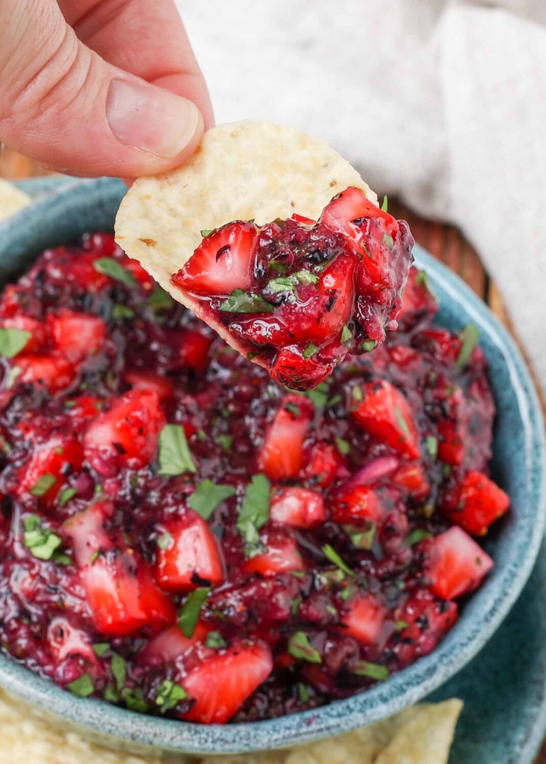 blueberry and strawberry salsa on a chip held by a hand over a blue bowl