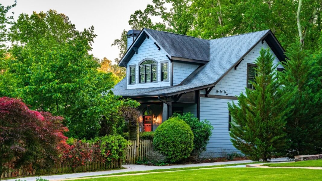 A light blue house surrounded by diverse year-round foundation plants including a red-leafed shrub, a spherical green shrub, and a conical evergreen.