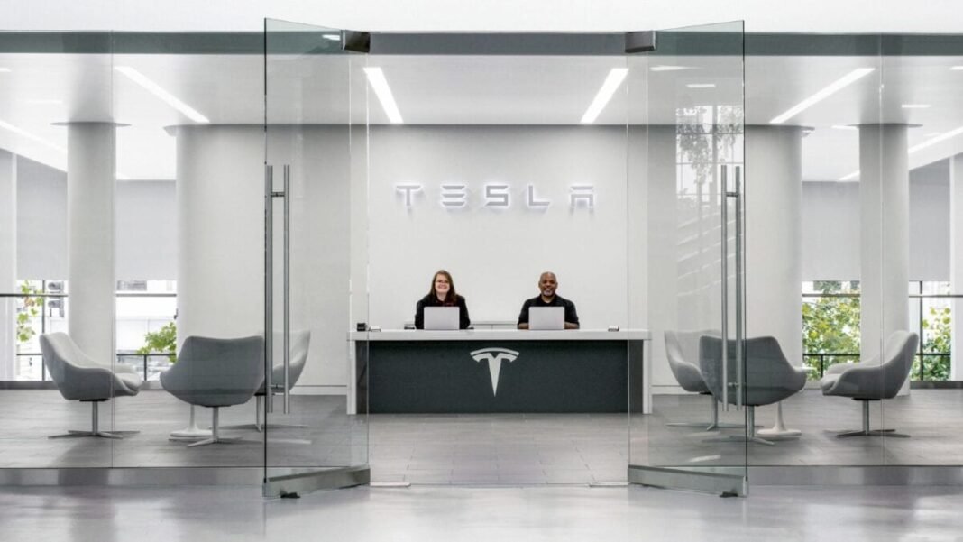 Two employees sat at desk welcoming customer to a Tesla car showroom