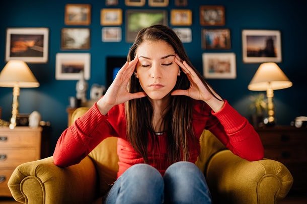 Woman in her living room overthinking and looking a bit stressed.