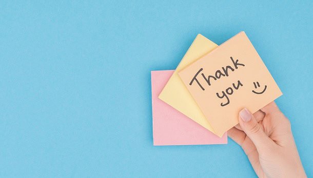 A hand holding up a note saying: Thank you :)