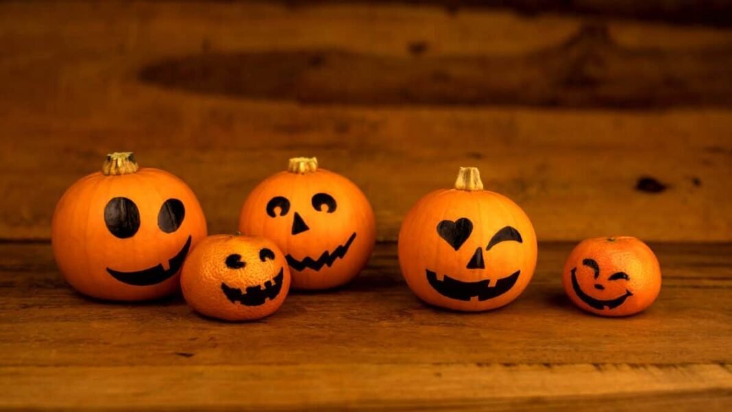 Little pumpkins and mandarines with painted faces for Halloween on wooden background