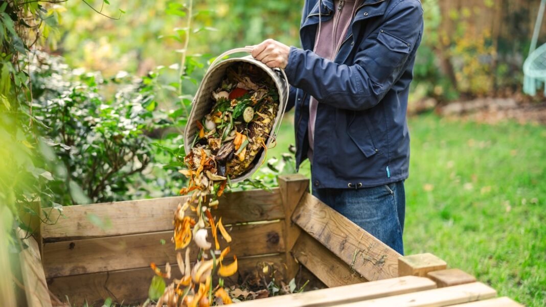 A gardener tosses fresh vegetable scraps into a compost container in the garden, illustrating practical fall compost tips for enriching soil.