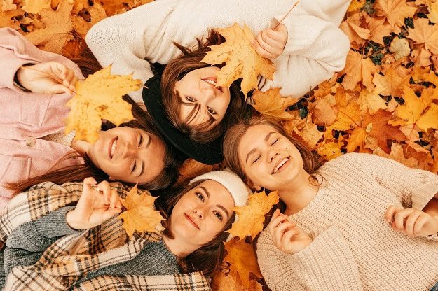 Smiling women lying on the ground in fall leaves.