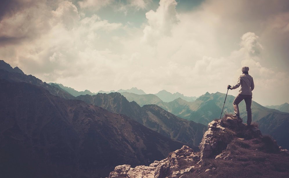 A woman who has climbed a mountain peak looking out at the impressive view.