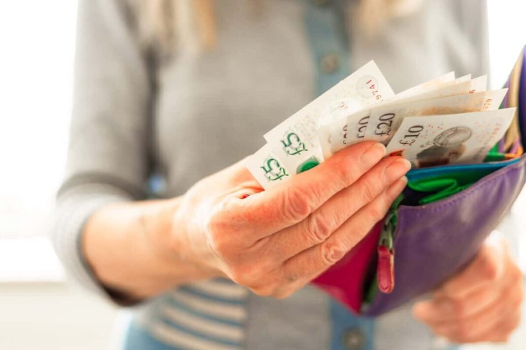 Close-up image depicting a woman in her 70s taking British bank notes from her colourful leather wallet.