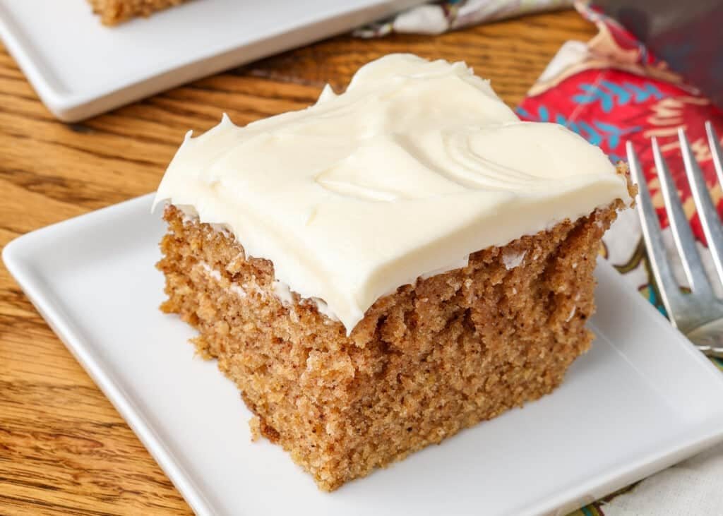 A slice of Crazy Spice Cake sits on a square white plate over a wooden tabletop. 