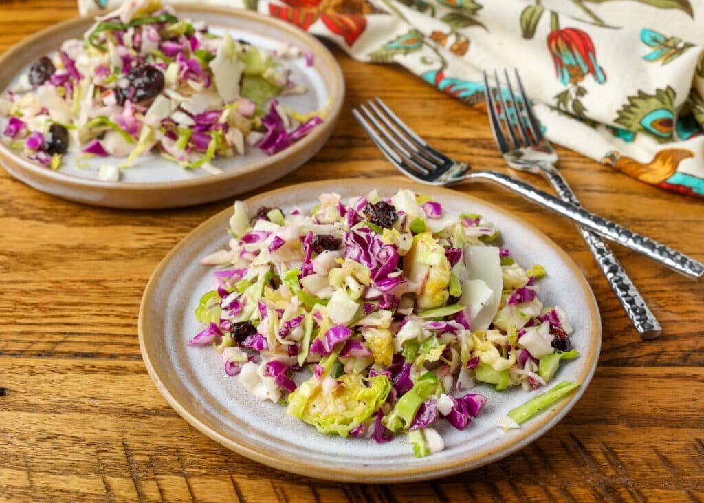 A horizontally aligned image of a ceramic plate piled high with shredded cabbage and sliced Brussels sprouts. 