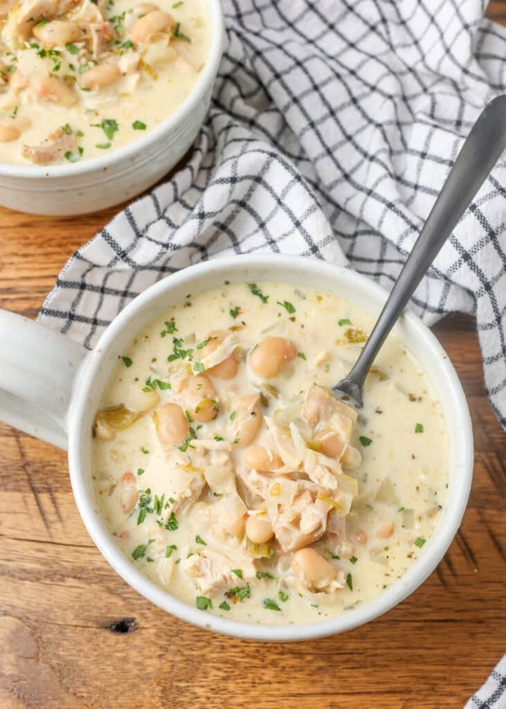 overhead photo of creamy chicken chili in white mug with black spoon on wooden table