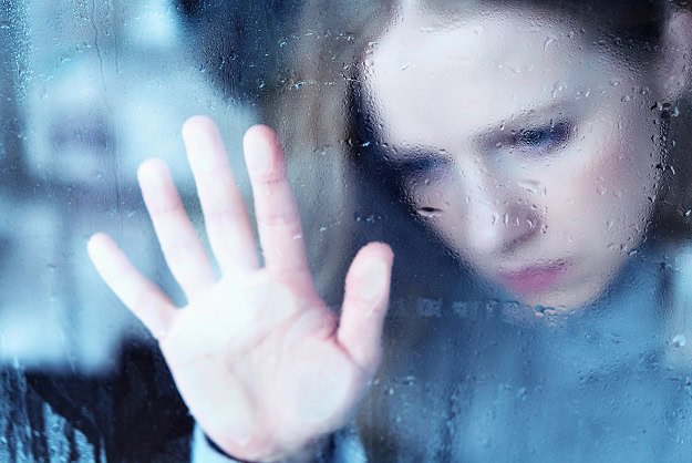 A sad woman putting her hand on a rainy window.