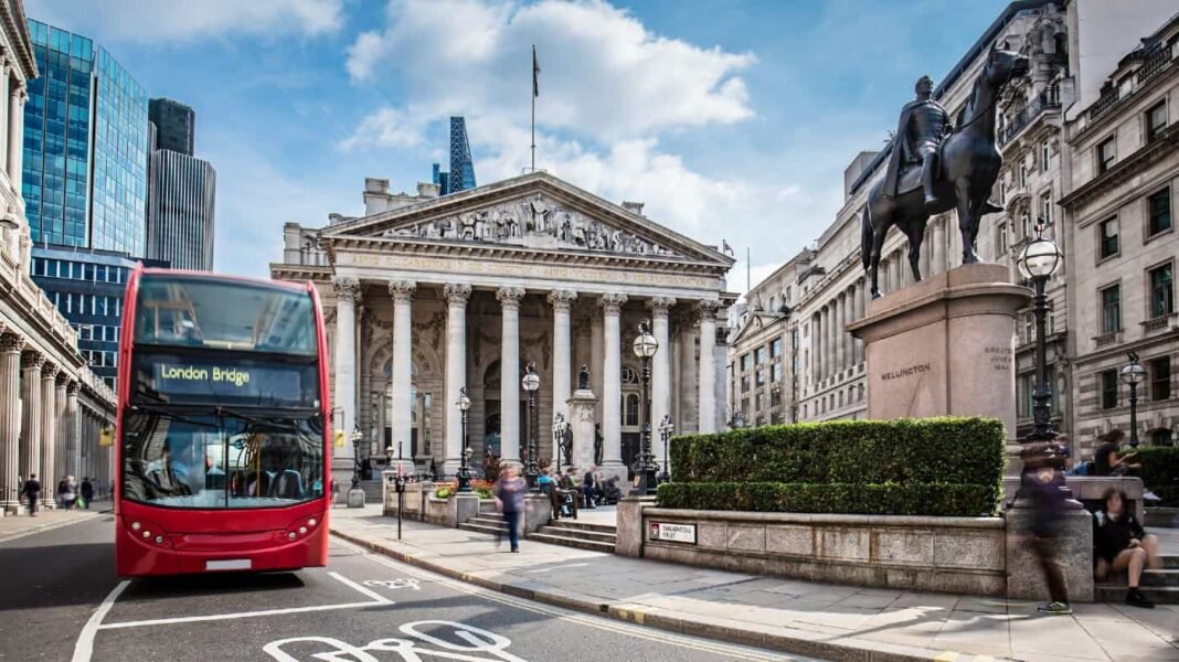 Two great UK stocks to consider in your March Stocks Bus waiting in front of the London Stock Exchange on a sunny day.