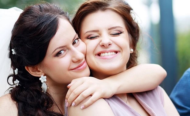 A woman hugging another woman while both are smiling.