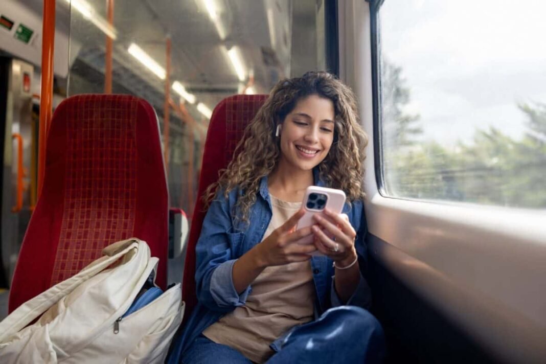 2 very cheap stocks to consider buying for your ISA Happy woman commuting on a train and checking her mobile phone while using headphones