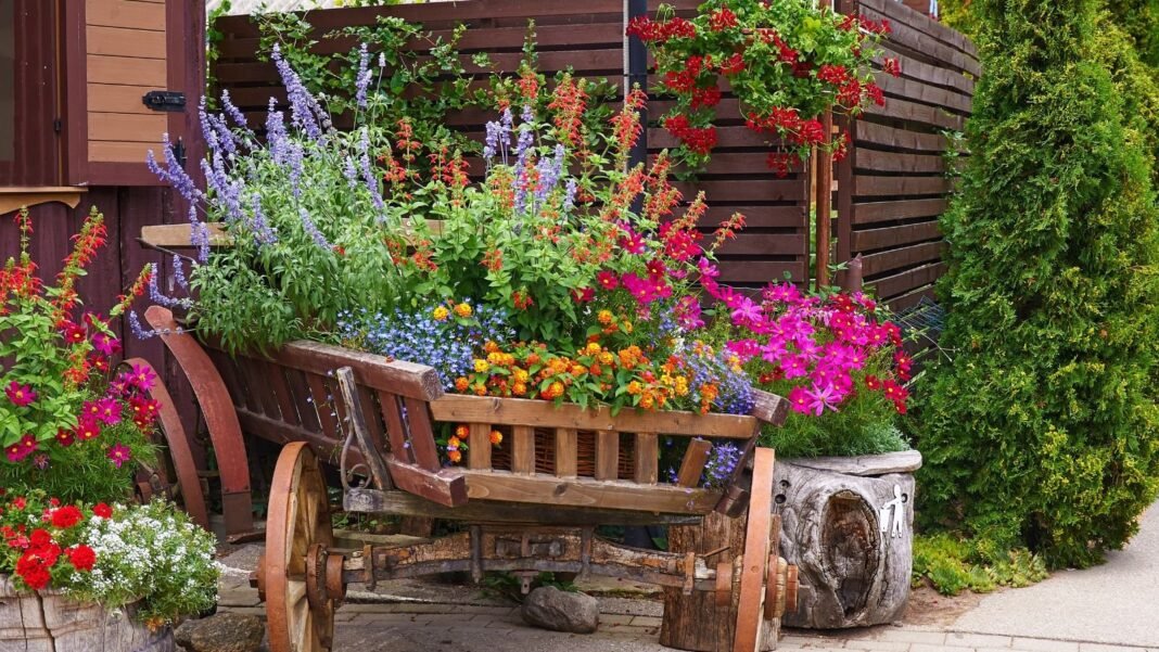 A close-up shot of a makeshift container made from a wagon and other small planters, all filled with various plants and flowers, showcasing cottage garden pots