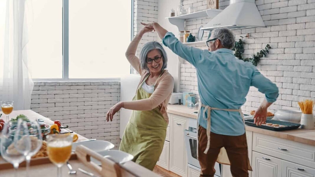 Is April 2026 the best time to buy Lloyds shares? Playful senior couple in aprons dancing and smiling while preparing healthy dinner at home