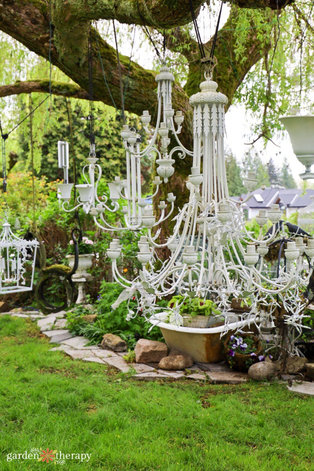 white chandeliers hanging from a mossy tree in the garden