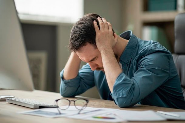 Man looking stressed and upset while sitting at his work desk.
