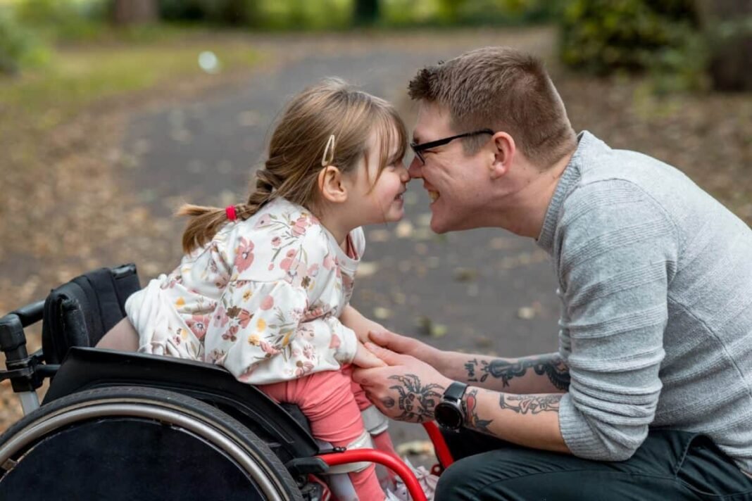 How much do I need in an ISA to earn A close up side view of a father and his young daughter who is a wheelchair user having a cute affectionate moment with each other whilst on a family day out in a beautiful public park in Newcastle upon Tyne in the North East of England.