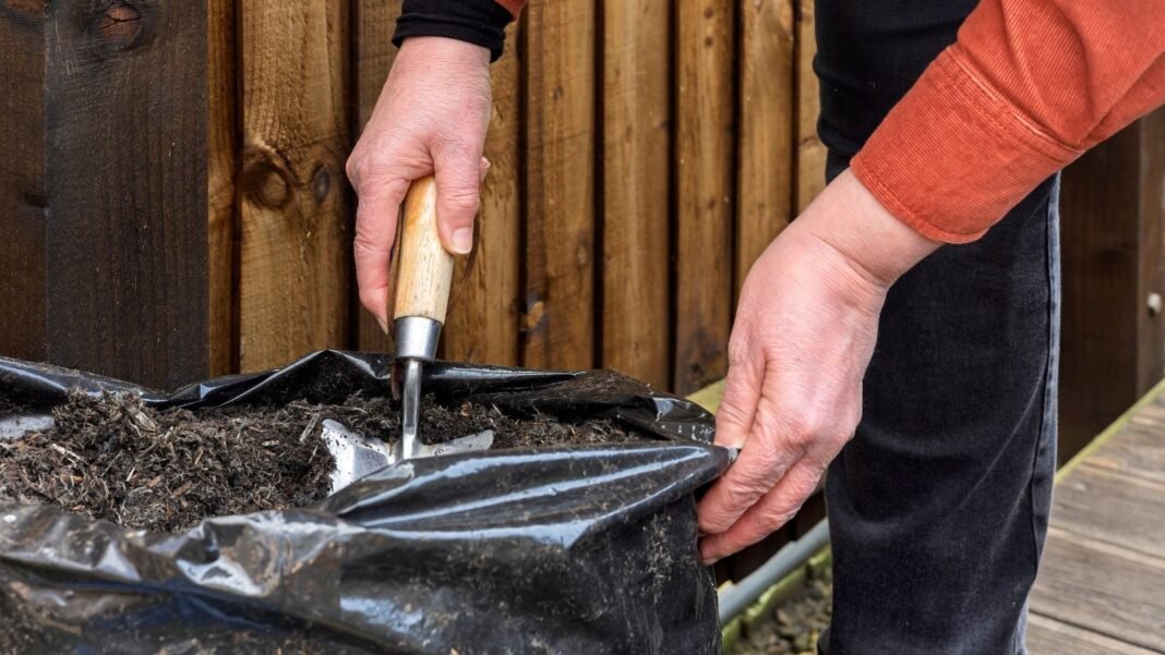 A person digging through bagged soil risks, using a trowel to work dark brown material inside a black plastic bag