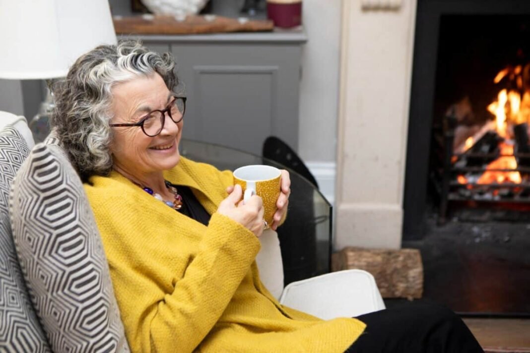 Can you finally stop worrying about the stock market crash A mature adult sitting by a fireplace in a living room at home. She is wearing a yellow cardigan and spectacles.