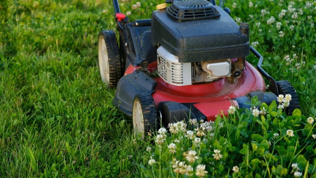 A close-up shot of a turned off red, colored mower beside flowering weeds, showcasing no mow May