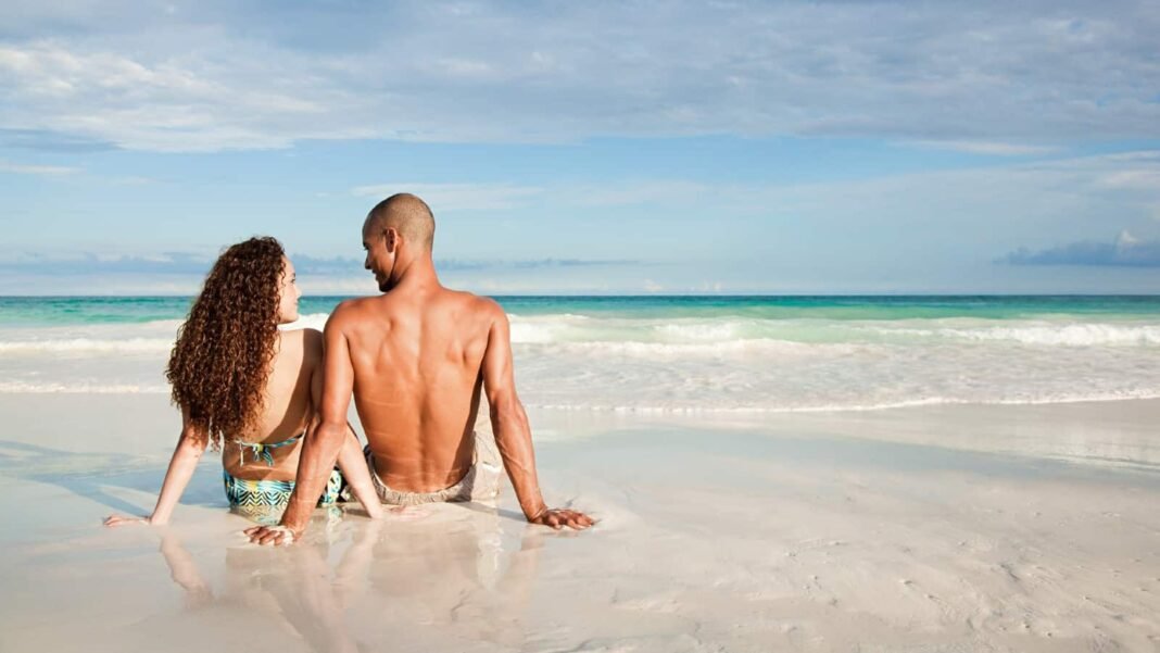 How much passive income do you need from your ISA Young mixed-race couple sat on the beach looking out over the sea