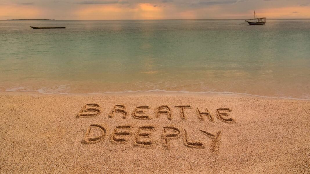 How oil price fluctuations are affecting stock market sentiment and A beach at sunset where there is an inscription on the sand "Breathe Deeeply".