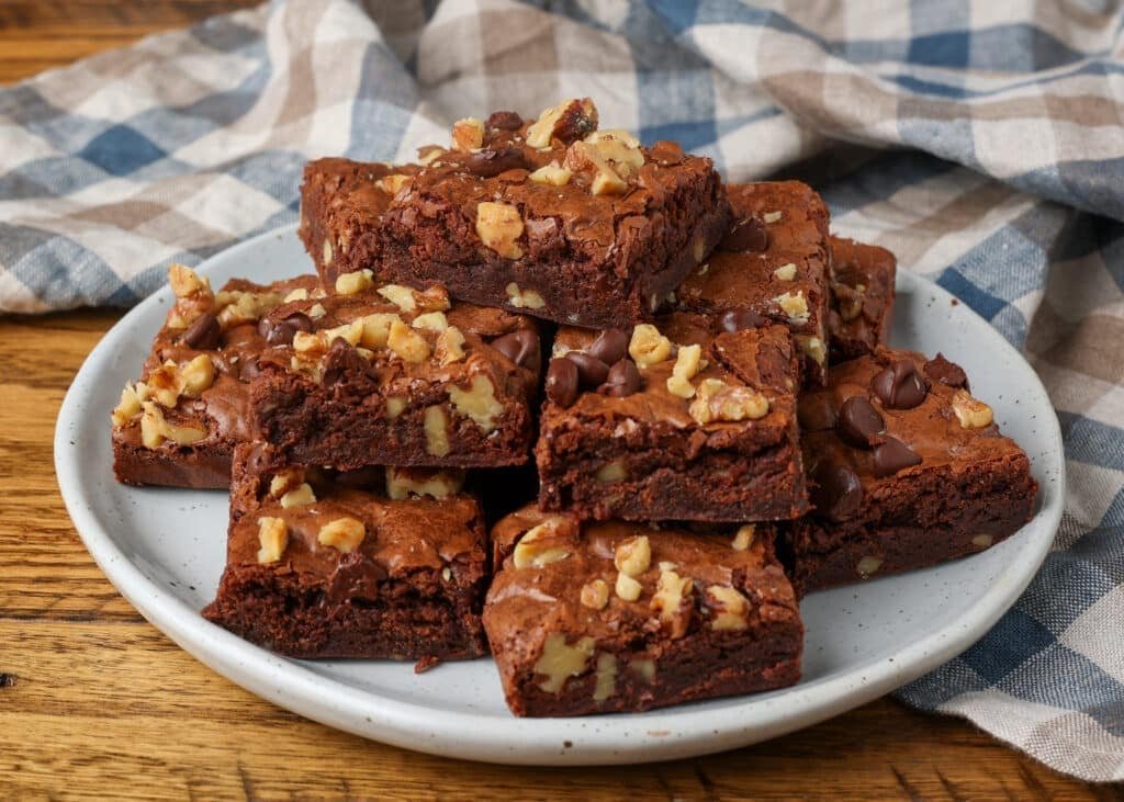 A close up shot of a pyramid of stacked brownies on a white plate over a wooden tabletop.
