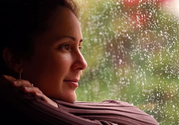 how_to_stop_daydreaming_2024.jpg Woman looking out of rainy window with a slight smile on her face.